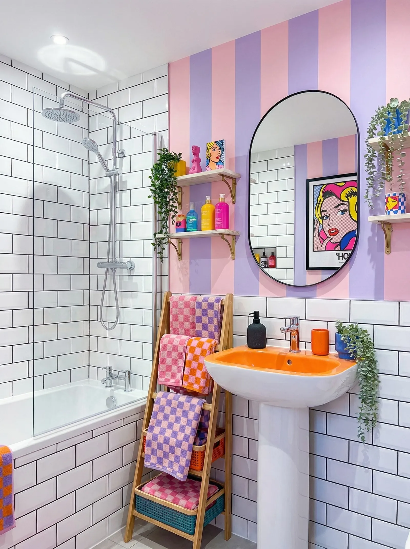 Pop art bathroom with white subway tile, pink and lilac striped wall, an orange pedestal basin and comic-style prints