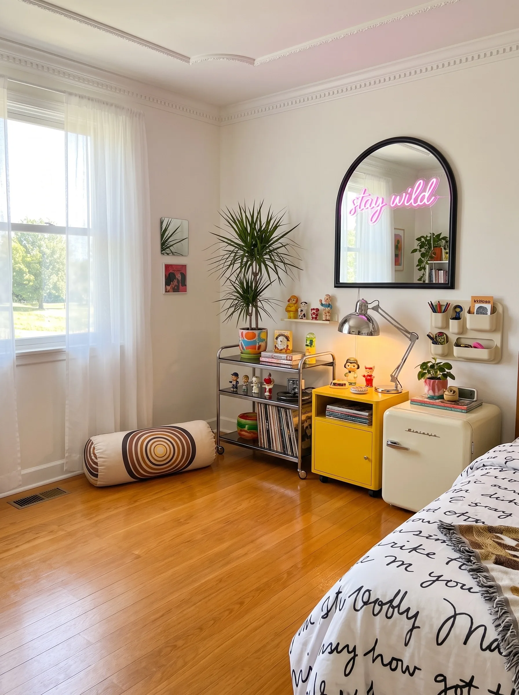 Bedroom with a script-print duvet, a chrome bar cart, a yellow metal cabinet, a mini fridge, a neon script mirror, figurines on shelves and plants in daylight