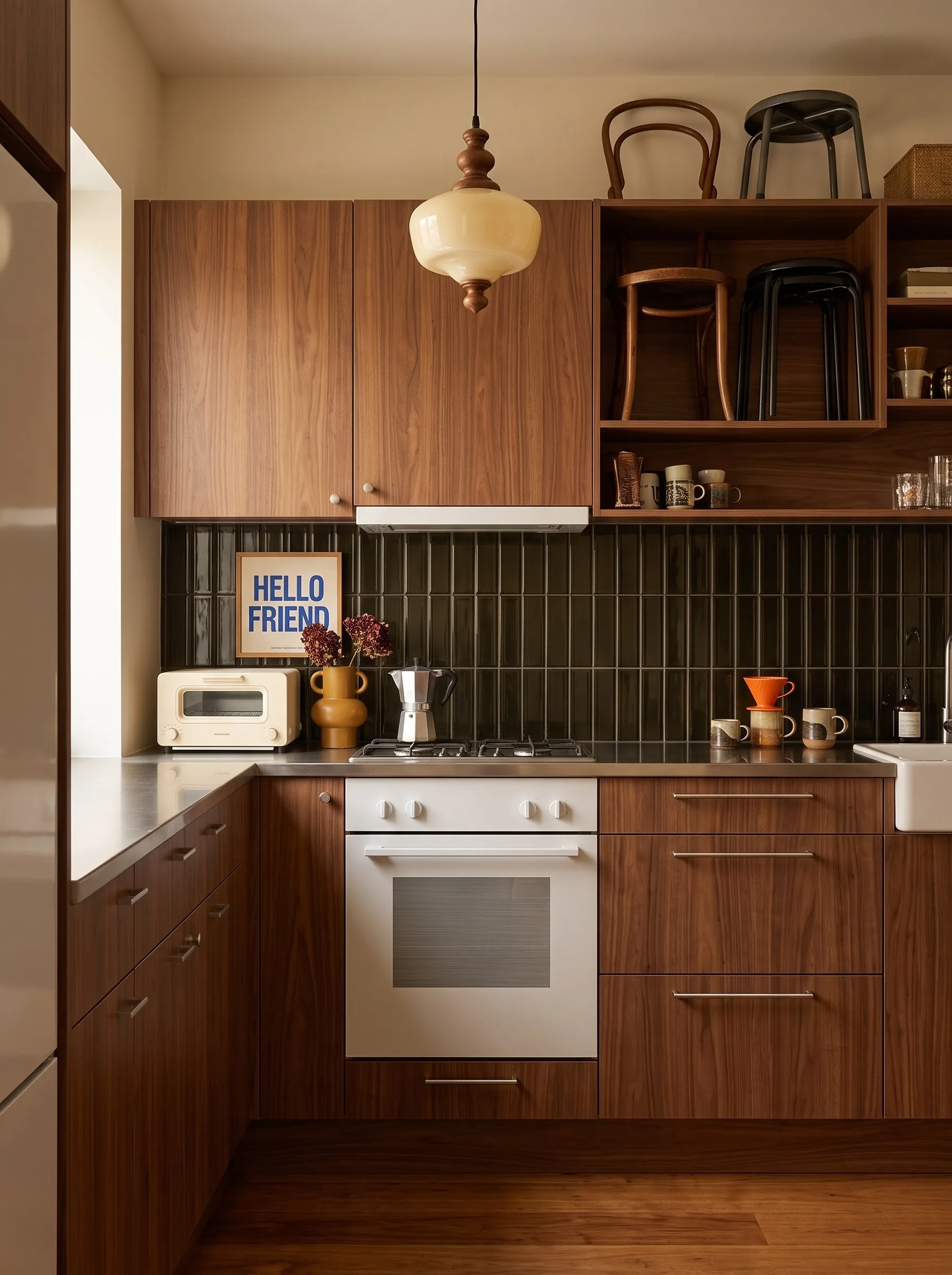 Kitchen with walnut slab cabinet doors, glossy near-black vertical stacked tile, a stainless steel worktop, a black cone pendant and open walnut shelves with retro mugs
